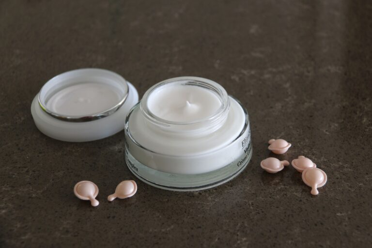 Open jar of luxurious face cream with capsules on a dark textured surface for skincare routines.